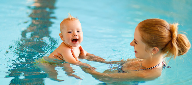 Bebê nadando na piscina com a mãe