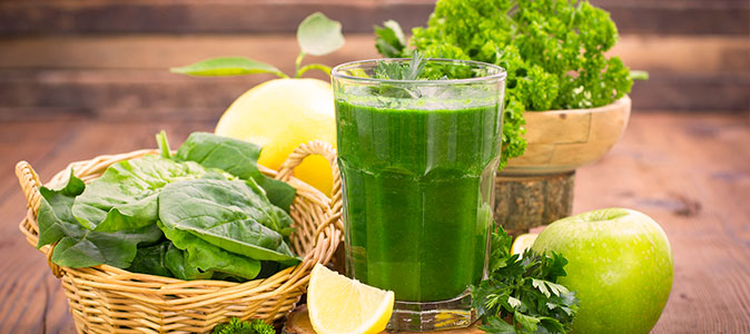 Imagem de um suco verde rodeado de verduras