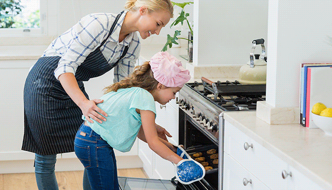 troca de 2 imagens, imagem 1: mãe ajudando filha colocar biscoitos no forno, imagem 2: foto de um menino cortando cebolas na cozinha com a ajuda de uma pessoa